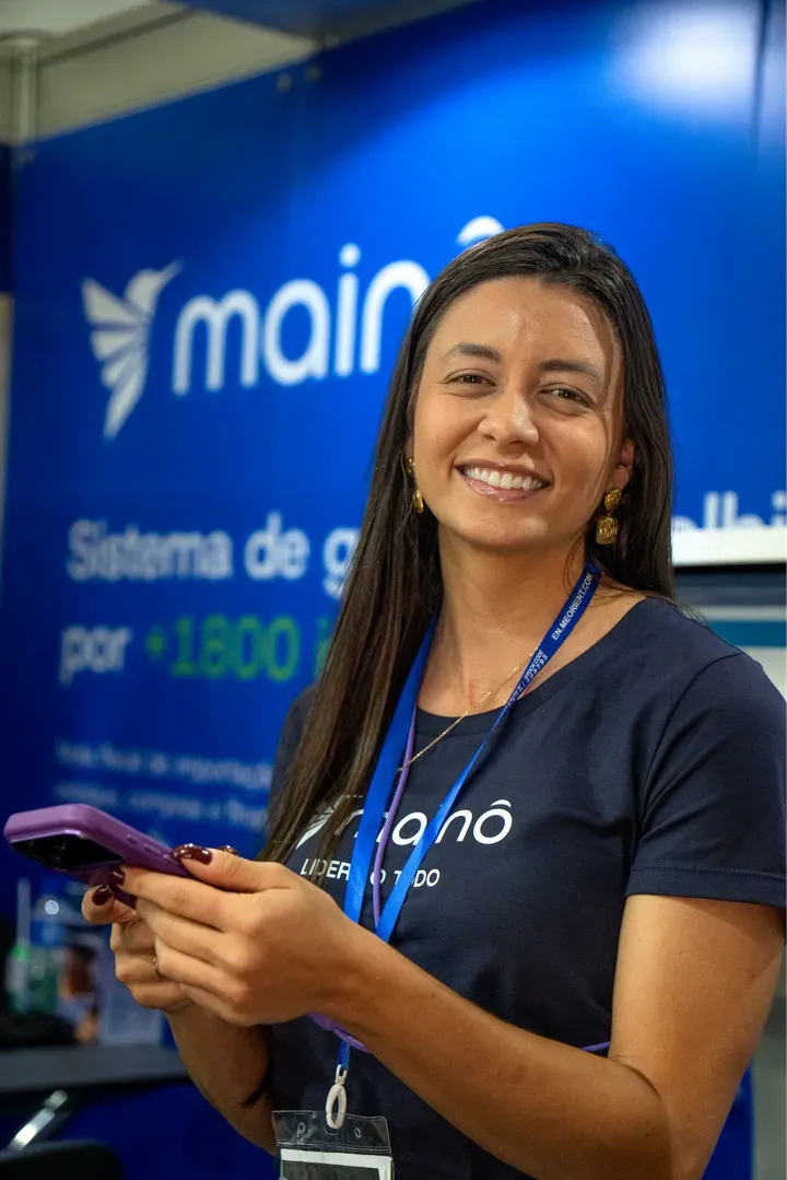 Colaboradora da Mainô sorrindo no estande da marca, com o crachá do evento