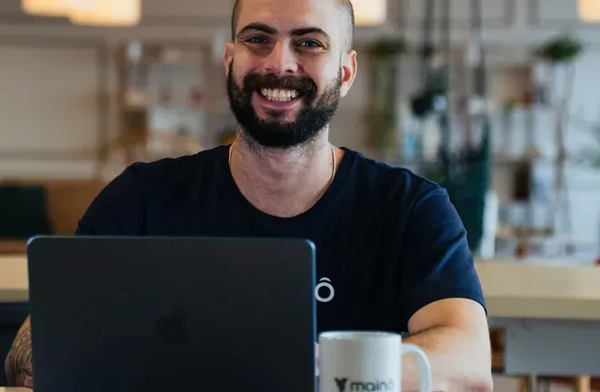 Colaborador da Mainô sorrindo atrás do notebook no escritório