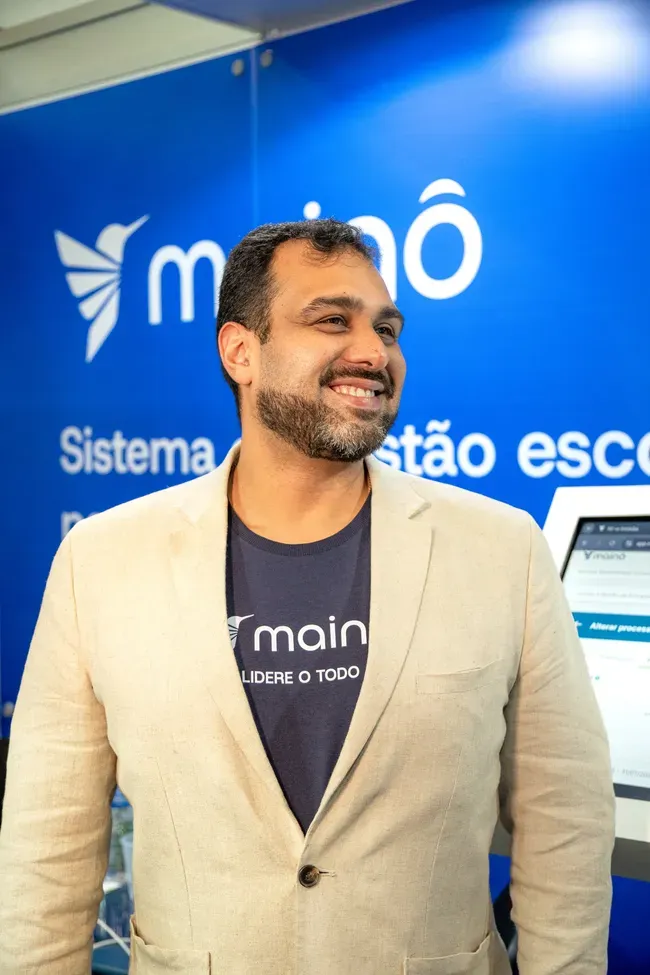 Colaborador da Mainô de blazer, sorrindo no estande da marca