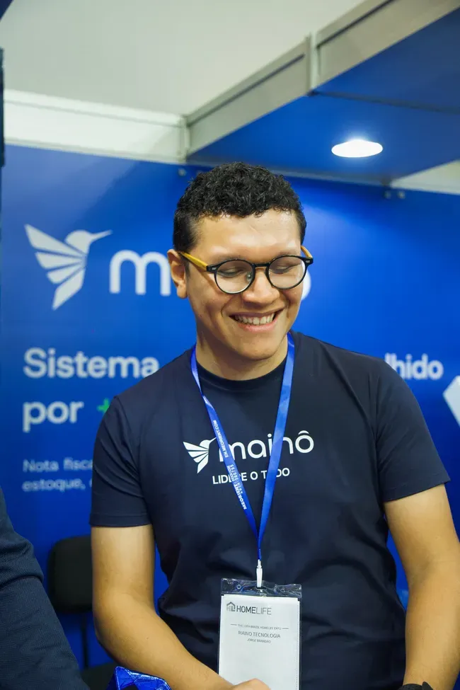 Colaborador da Mainô de óculos, sorrindo no estande da marca