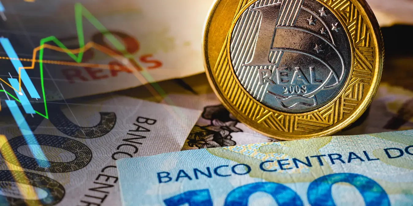 Moeda de 1 real em pé sobre notas de 100 e 200 reais, com um gráfico de cotação sobreposto