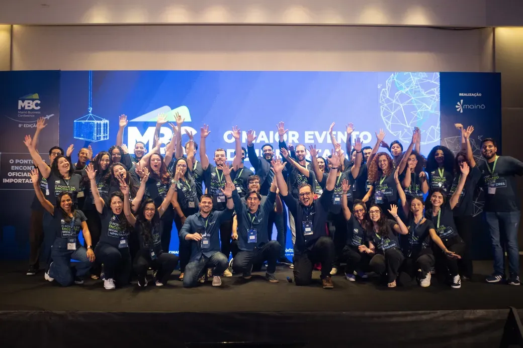 Time da Mainô reunido no palco do Mainô Business Conference, com os braços para cima